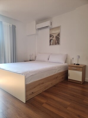 Une chambre à coucher moderne avec un lit en bois, une table de chevet, une commode et un climatiseur fixé au mur.