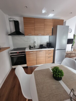 A modern kitchen with wooden cabinets, a stainless steel range hood, a built-in oven, and a refrigerator.