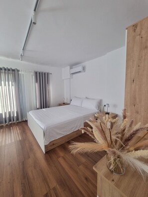 Une chambre à coucher moderne avec un plancher en bois, un lit blanc, une table de chevet et une plante décorative.