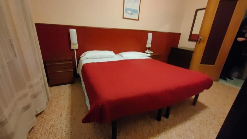 A hotel room with a bed, bedside tables, and a door.
