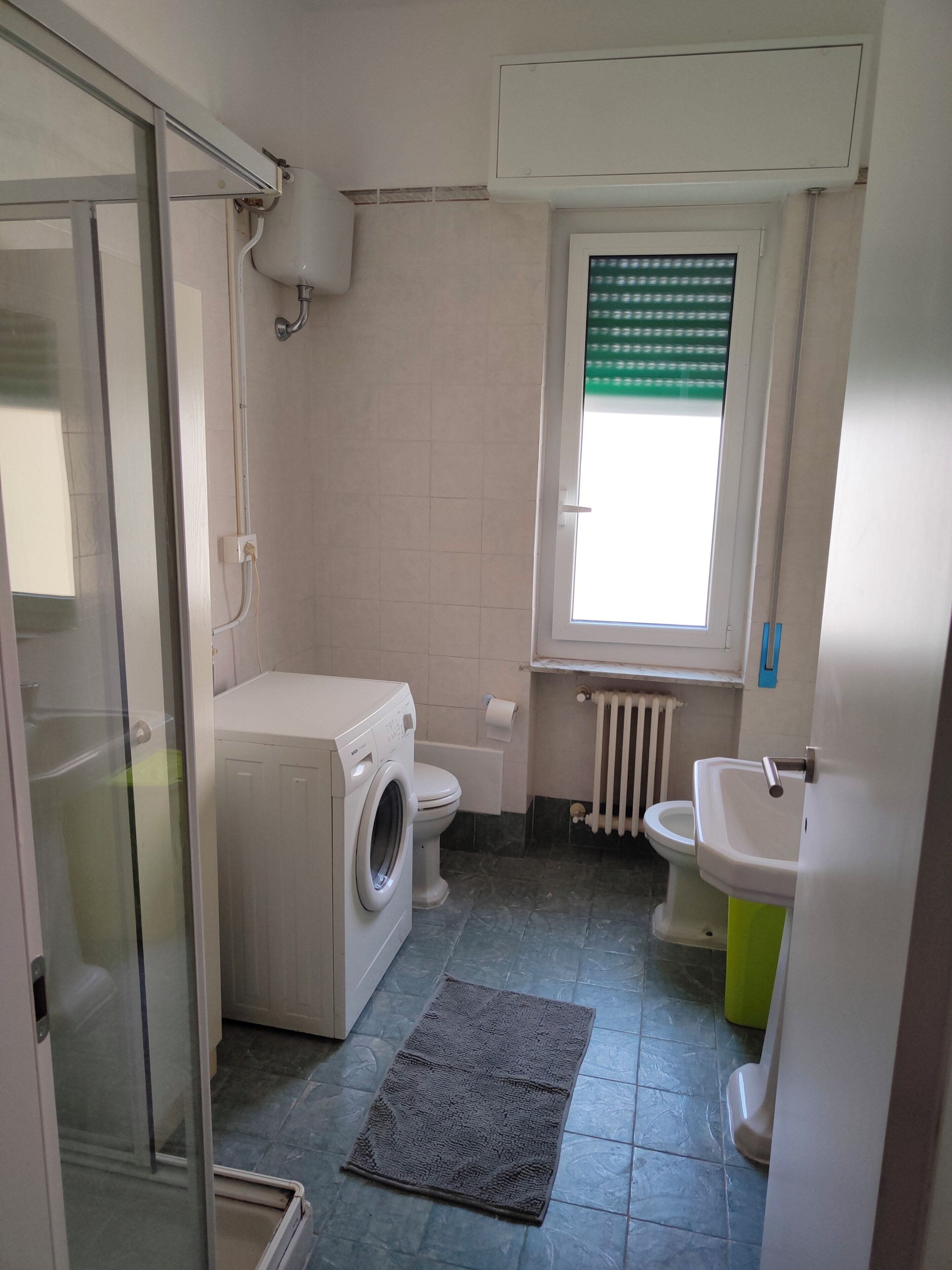 A compact bathroom with a washing machine, toilet, radiator, and sink.