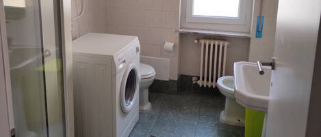 A compact bathroom with a washing machine, toilet, radiator, and sink.