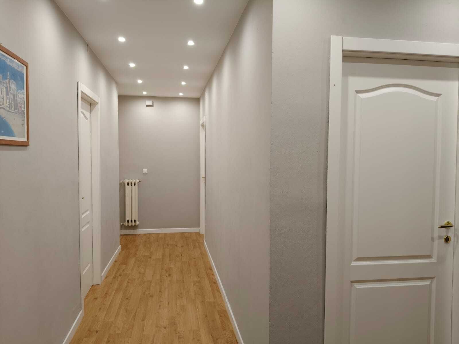A hallway with wooden flooring, white walls, and a white door on the right.