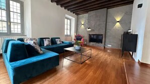 A spacious living room with a wooden floor, a blue sofa set, a coffee table, a fireplace, and a TV. - Villa Magnolia Como (Como)