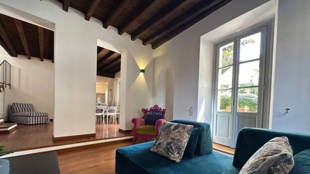 A modern living room with a blue sofa, a dining area with a white table and chairs, and a large window with a view of greenery. - Villa Magnolia Como (Como)
