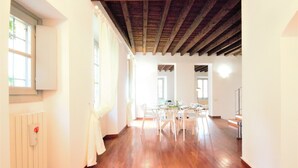 A spacious room with wooden flooring, a dining area with white chairs, and a ceiling with exposed beams. - Villa Magnolia Como (Como)