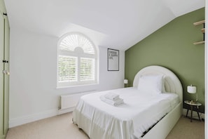 A bedroom with a bed, a window with blinds, a radiator, a framed motivational quote, and a bedside lamp.