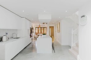 A modern kitchen with white cabinetry, a central island, and a dining area with chairs.