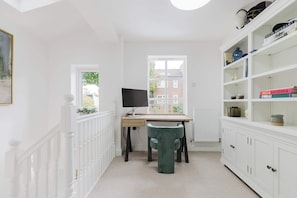 A room with a desk, chair, bookshelf, and a window with a view of buildings.