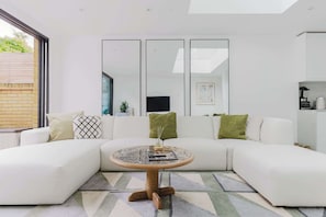 Una sala de estar moderna con un sofá seccional blanco, una mesa de centro redonda de vidrio y un ventanal grande.