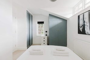 Un dormitorio con cama, ventana, armario y un cuadro en la pared.