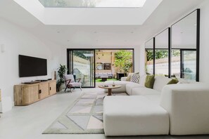 A modern living room with a flat-screen TV, a sofa, a coffee table, and a large window.