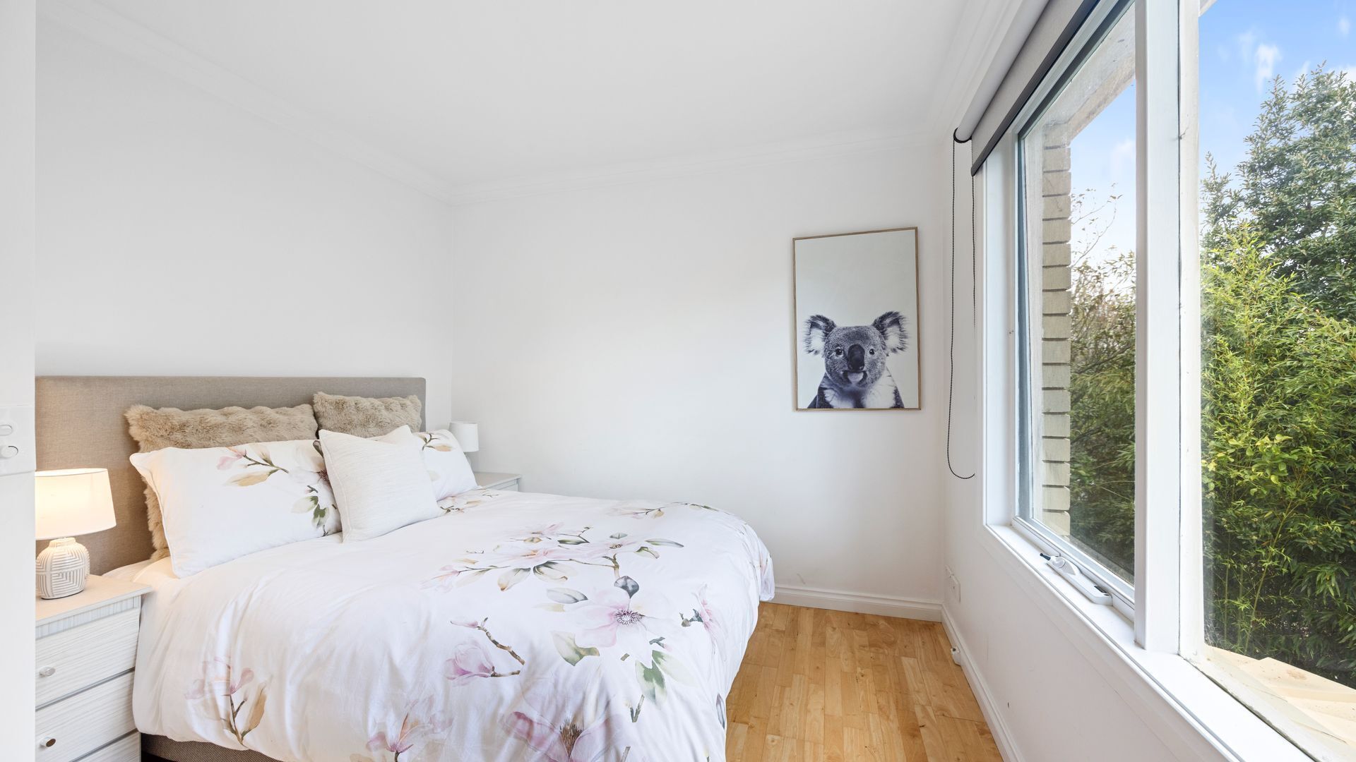 Une chambre à coucher avec un lit, une table de chevet, une lampe et une fenêtre donnant sur des arbres.