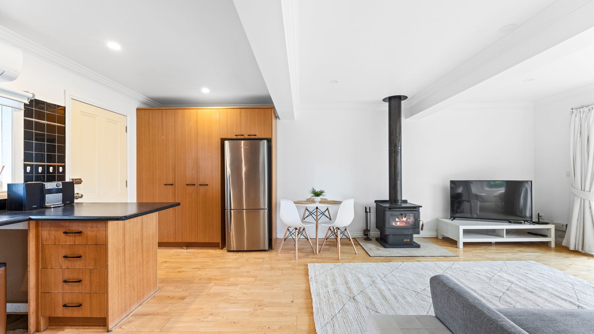 Une cuisine moderne avec des meubles en bois, un réfrigérateur en acier inoxydable et un coin repas comprenant une table et des chaises blanches.