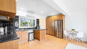 A modern kitchen with wooden cabinets, a stainless steel refrigerator, and a dining area with a white table and chairs. - Serene 2BR Retreat in Goughs Bay Lake Eildon (Goughs Bay)