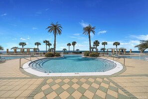 Une grande piscine aux eaux cristallines, bordée d’une terrasse carrelée et entourée de palmiers et d’une clôture blanche.