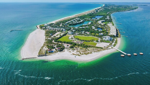 Vista aérea de un resort costero con una extensa playa, aguas azules cristalinas y una distribución ordenada de edificios y zonas verdes.
