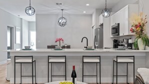 Una cocina moderna con una isla central, taburetes de bar, iluminación colgante y un comedor con una mesa redonda y sillas.