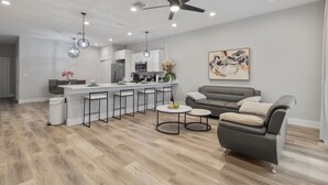 Una sala de estar moderna con un sofá gris, una mesa de centro y una zona de comedor con taburetes de bar.