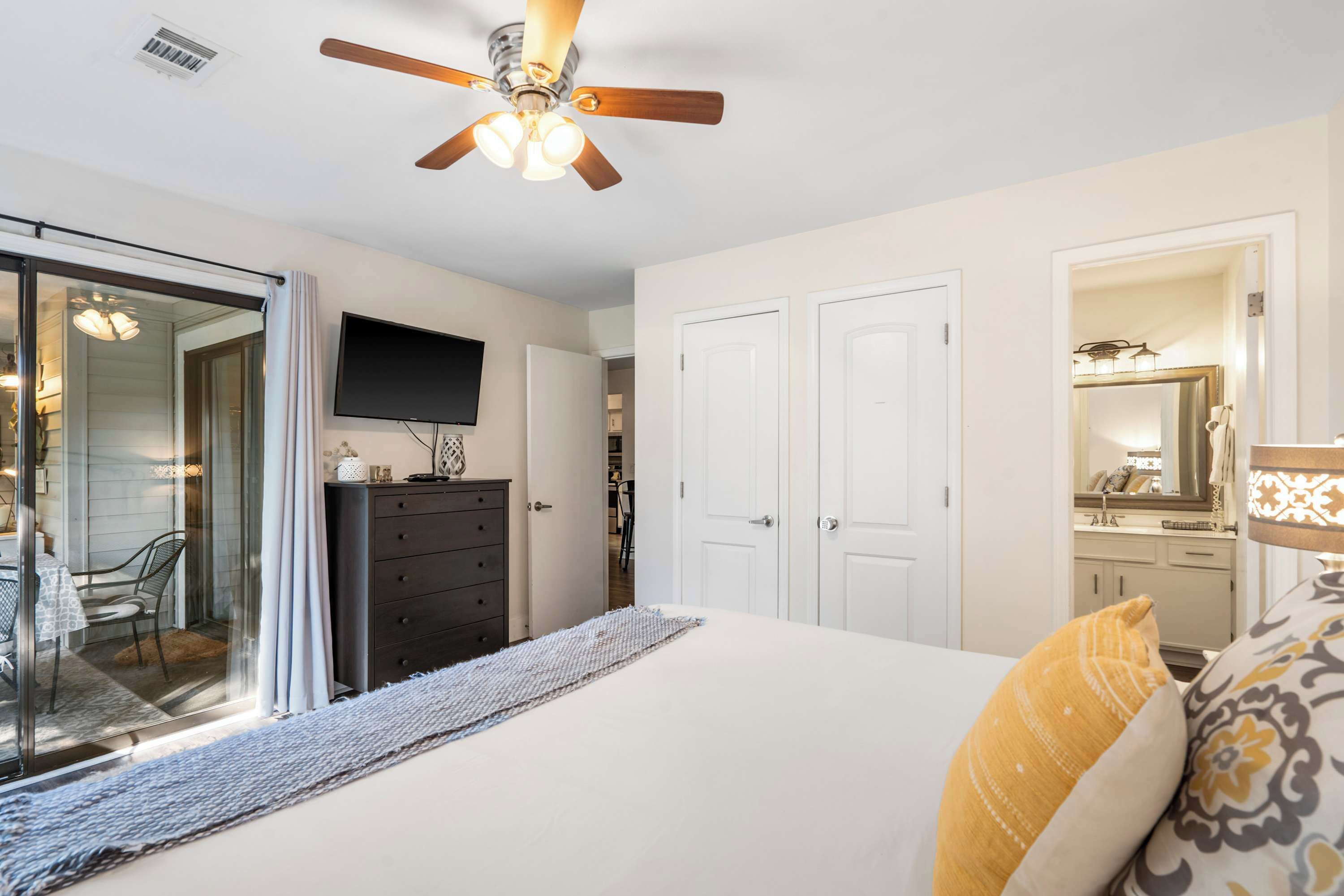 A bedroom with a bed, a dresser, a television, and a ceiling fan.