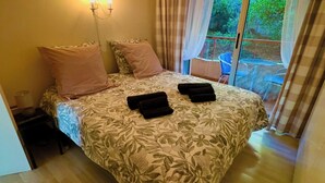 Une chambre à coucher avec un lit, une table de chevet, une lampe et une vue sur l’extérieur.