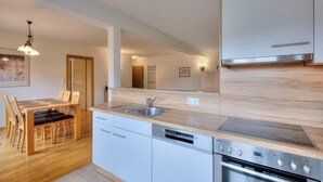 A modern kitchen with a wooden dining table, built-in dishwasher, stainless steel sink, and oven. - Vicky Apartment With Infrared Cabin (Wildschönau)