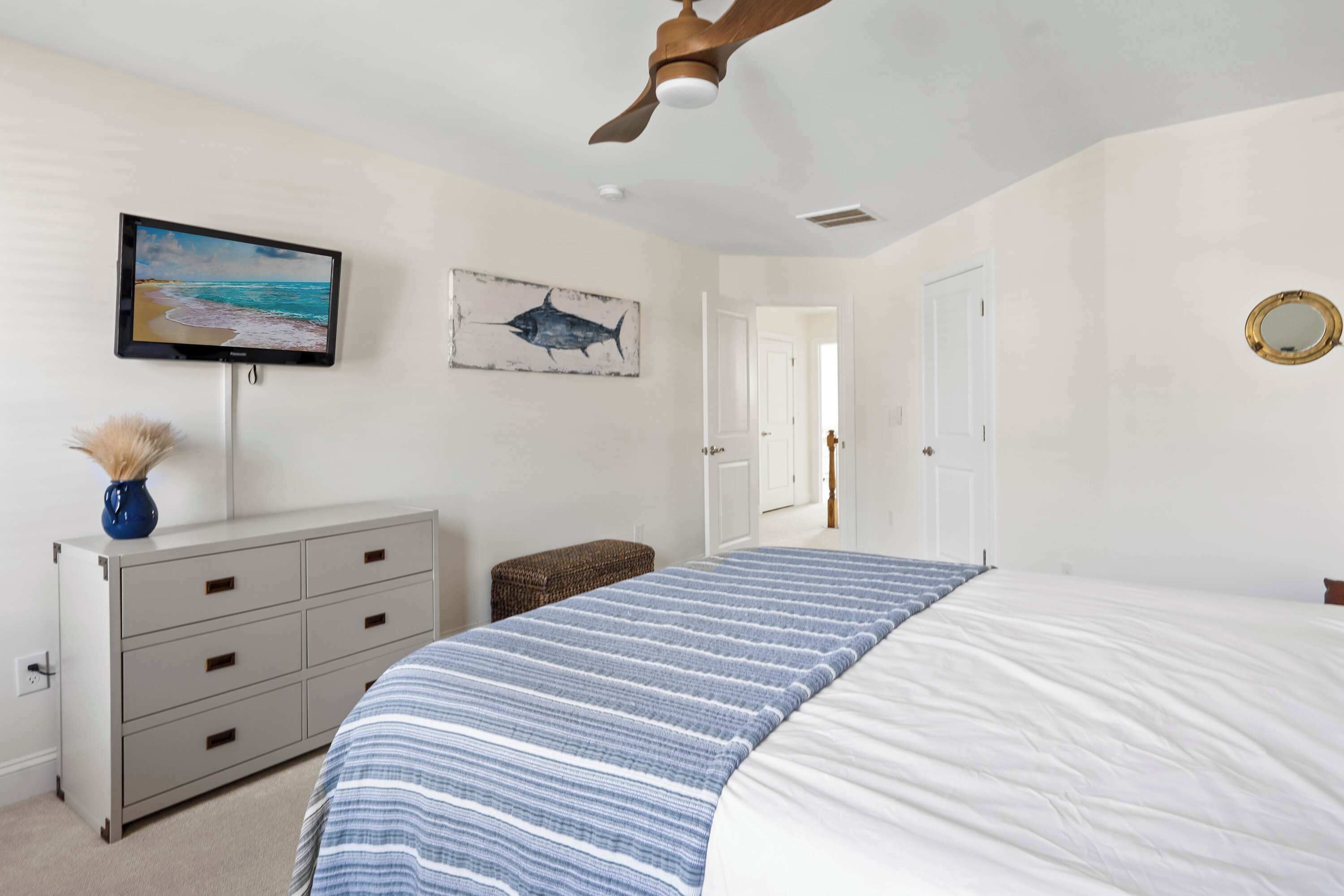 A bedroom with a bed, a dresser, a television, and a ceiling fan.