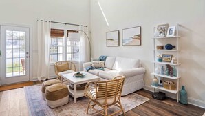 Un salon avec un canapé blanc, des fauteuils en osier, une table basse et une bibliothèque agrémentée d’objets décoratifs.