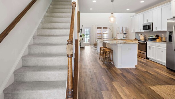 Une cuisine moderne dotée d’un îlot central, d’un escalier en bois et de meubles de rangement blancs.