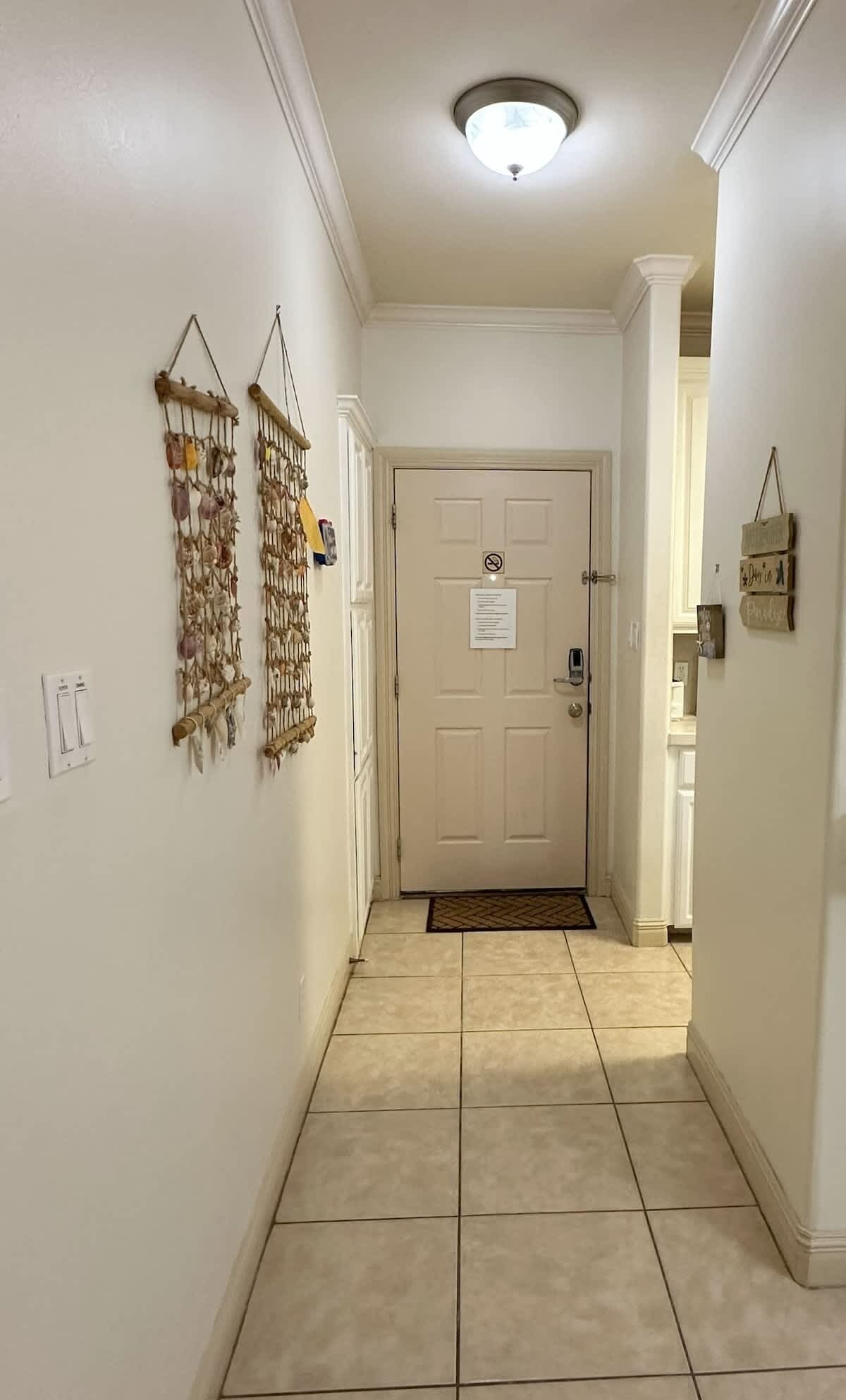 A hallway with a tiled floor, a light fixture on the ceiling, and a door with a sign above it.