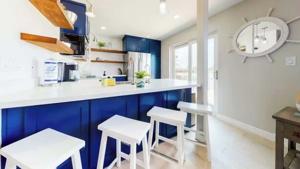 Une cuisine moderne avec des meubles bleus, des plans de travail blancs et des tabourets de bar.