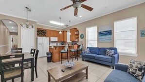 A modern living room with a blue sofa, wooden coffee table, and a dining area with a wooden table and chairs. - Lovely Beach and Pool Condo (South Padre Island)