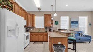 A modern kitchen with wooden cabinets, a white refrigerator, and a blue sofa in the living area. - Lovely Beach and Pool Condo (South Padre Island)
