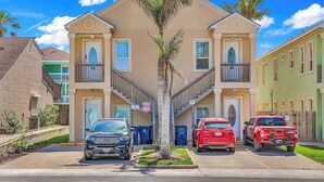 A multi-story residential building with a central staircase, parking spaces, and a palm tree in the middle. - Lovely Beach and Pool Condo (South Padre Island)