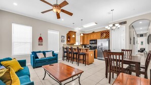 A modern living room with a blue sofa, wooden dining table, and a kitchen area with wooden cabinets and a refrigerator. - Your Ultimate Getaway Awaits in South Padre Island (South Padre Island)