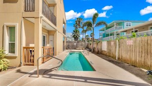A swimming pool with a wooden fence, a building with balconies, and palm trees in the background. - Your Ultimate Getaway Awaits in South Padre Island (South Padre Island)