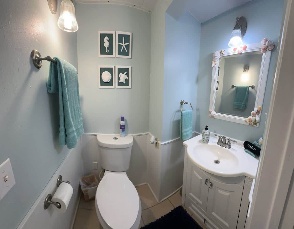 A bathroom with a toilet, sink, and towel rack. There are framed pictures on the wall and a mirror above the sink.