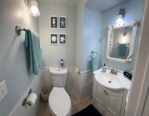 A bathroom with a toilet, sink, and towel rack. There are framed pictures on the wall and a mirror above the sink. - Lovely Cozy Cottage-pet Friendly (Port Isabel)