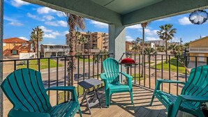 Un balcon avec des chaises vertes, une petite table et un barbecue.