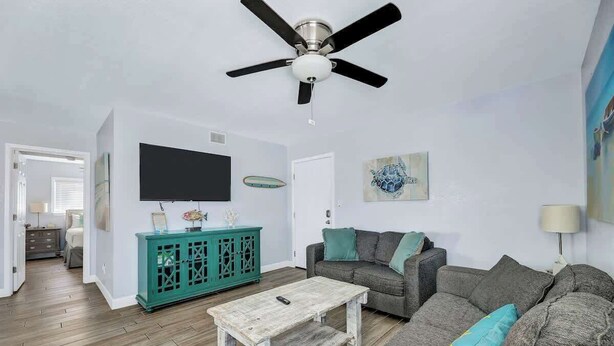 A living room with a ceiling fan, a television, a teal cabinet, and a gray sofa with teal cushions. - Gulf Coast Beach Front Condo (South Padre Island)