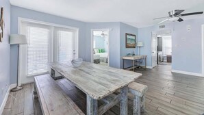 Une pièce spacieuse avec une grande table en bois et des bancs, des murs bleu clair et un ventilateur de plafond.