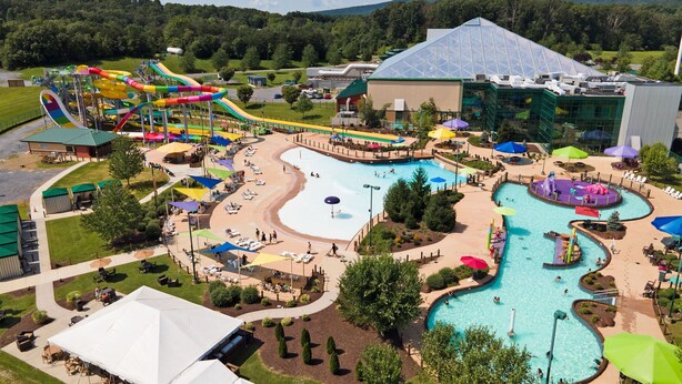 A water park with multiple slides and pools, surrounded by trees and a large building with a glass roof. - Peak Seasons at Massanutten (Mc Gaheysville)