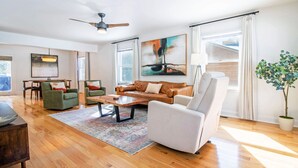 A spacious living room with a wooden floor, a brown leather sofa, a white armchair, a coffee table, and a large abstract painting. - Peak Seasons at Massanutten (Mc Gaheysville)