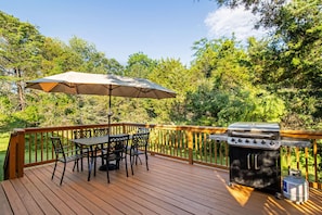 Eine Terrasse mit Grill, Tisch, Stühlen und Sonnenschirm.
