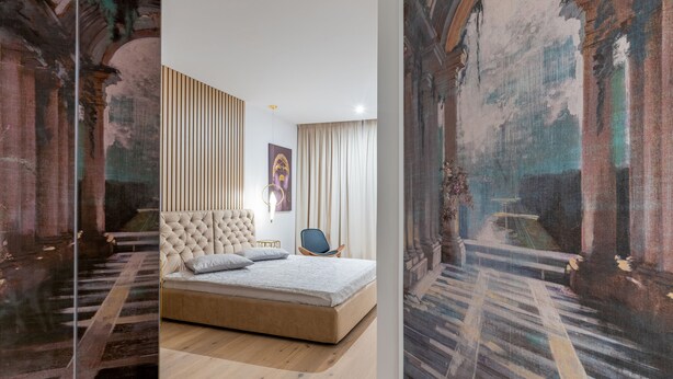 Quarto com uma cama grande, uma cadeira, um quadro e um candeeiro fixado na parede.