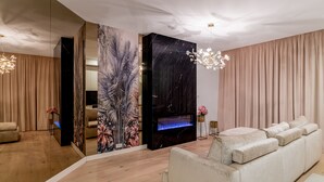 Uma sala de estar moderna com um sofá branco, um grande mural na parede, uma lareira e um lustre.