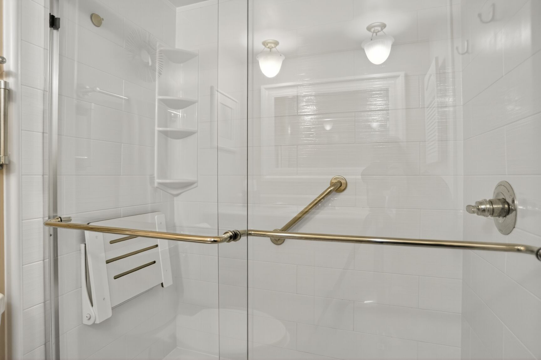 A modern shower with a glass door, a handrail, and a white tiled wall.