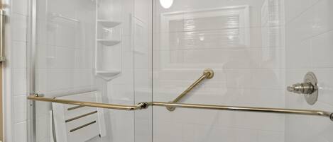A modern shower with a glass door, a handrail, and a white tiled wall.