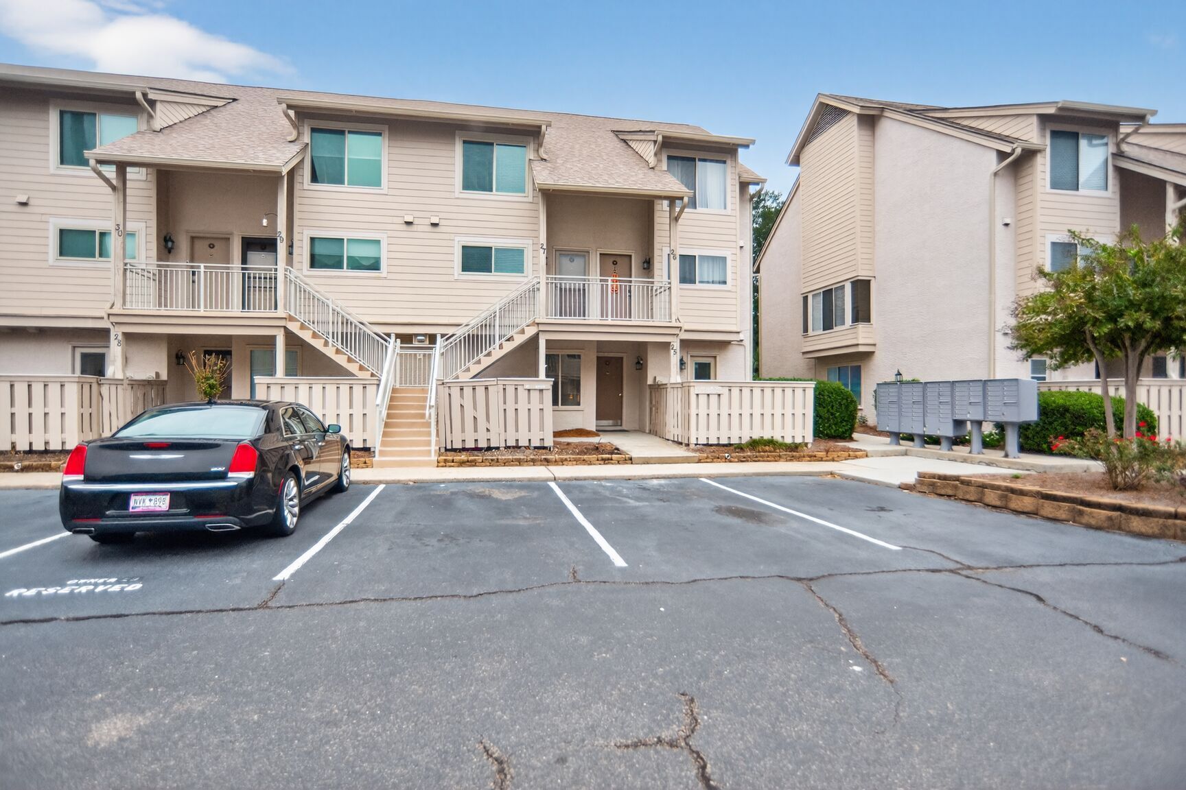 A multi-story apartment building with a parking lot, a car, and a mailbox.