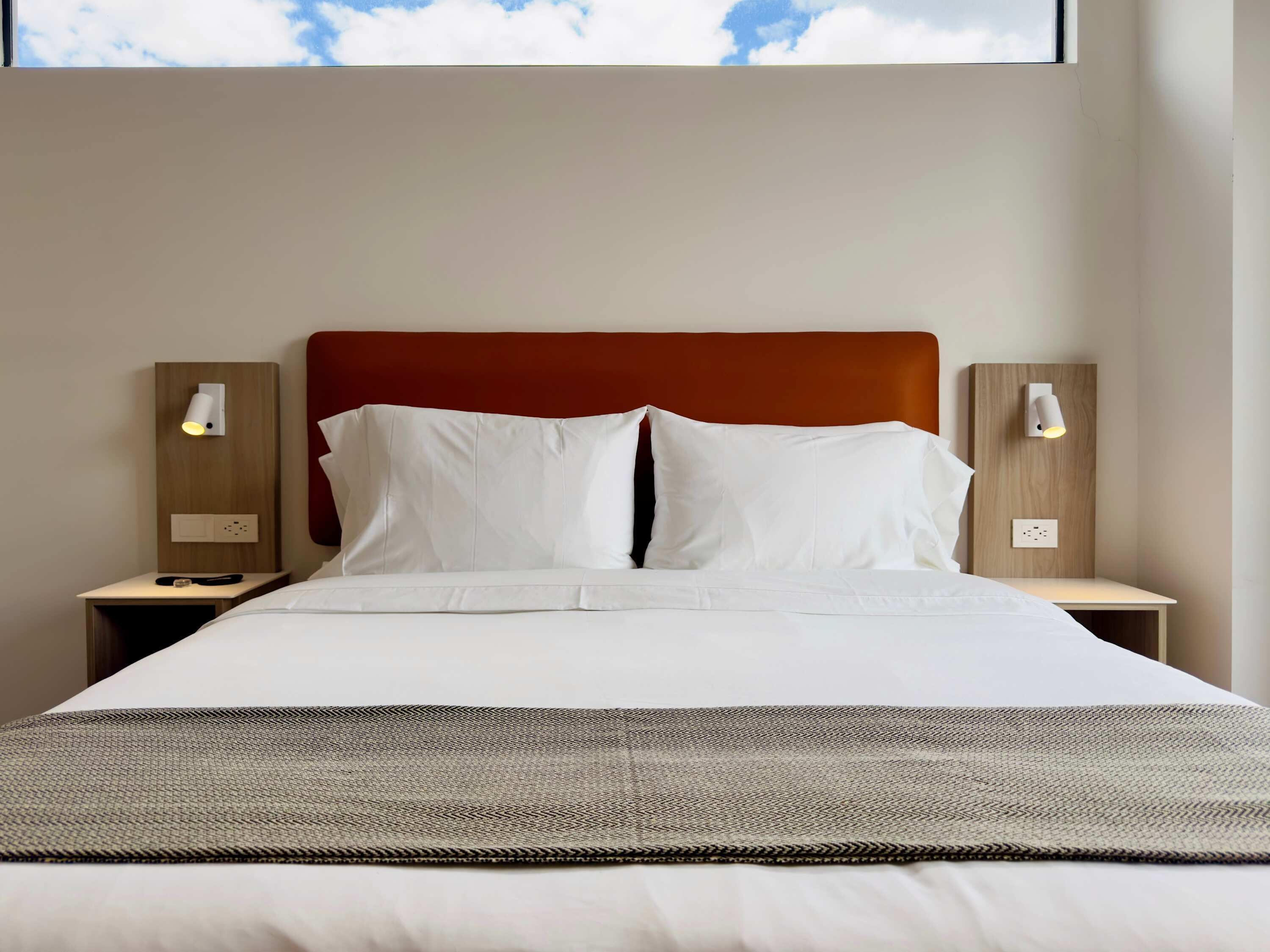 Ein Hotelzimmer mit einem großen Bett, einem Holzkopfende, zwei Nachttischen und einem Fenster mit Blick zum Himmel.